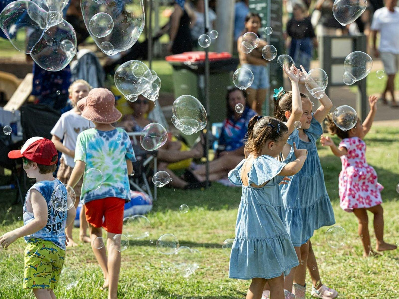 Children playing outdoors and chasing bubbles.