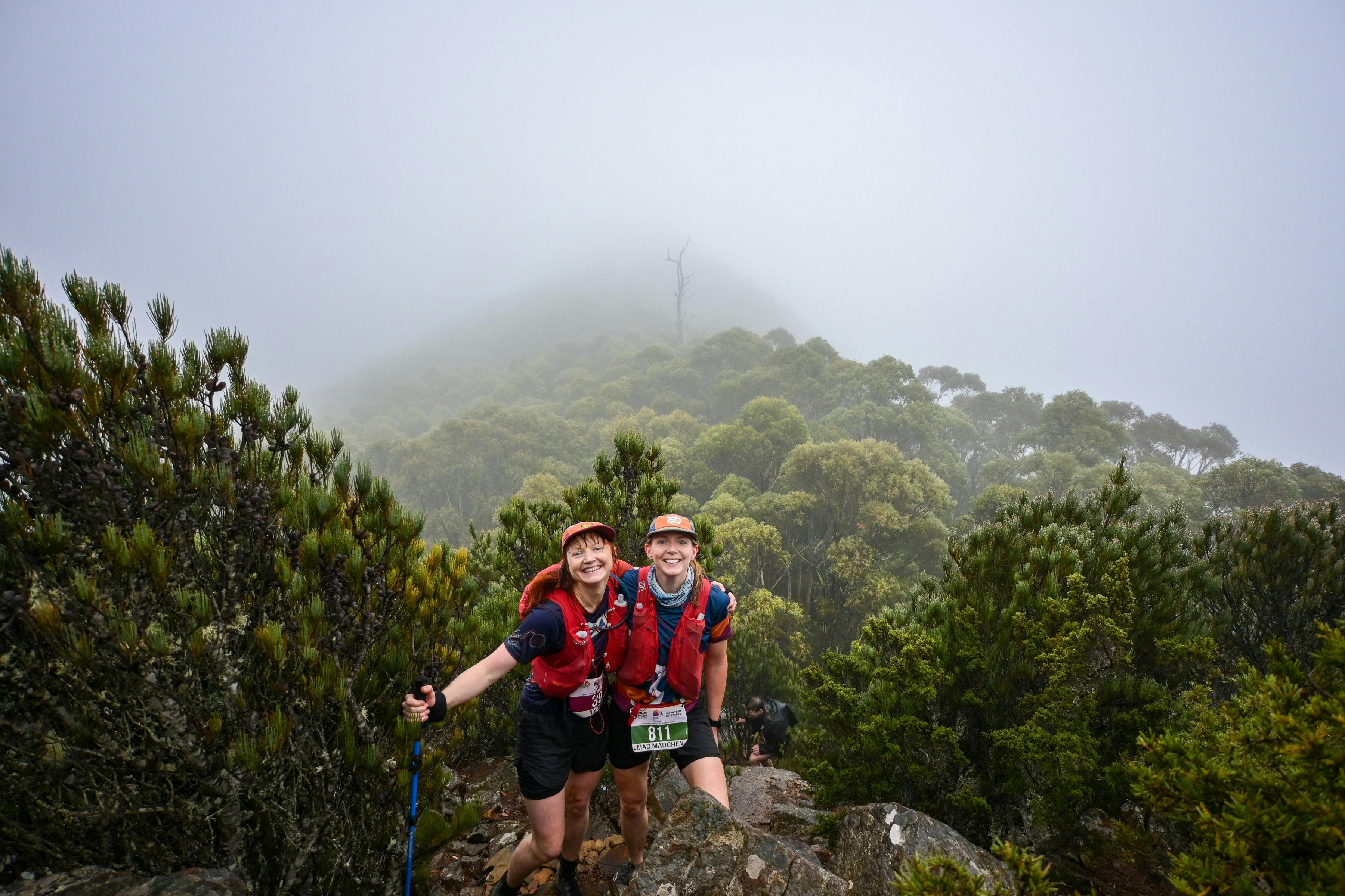 Two female runners pose for a photo with a misty landscape behind them