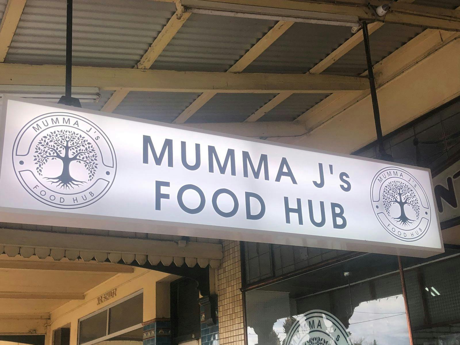 Mumma J's Food Hub white glowing sign hanging from the roof outside of the shop.