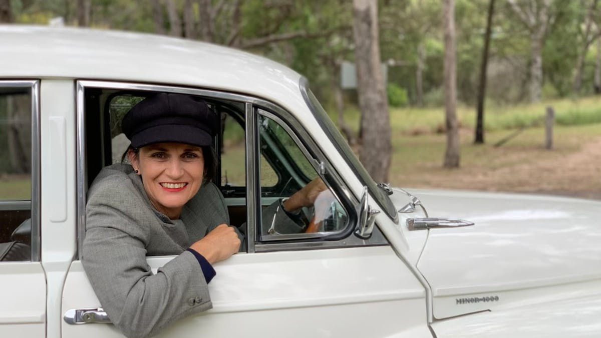 Woman smiling, looking out open car window, wearing a hat