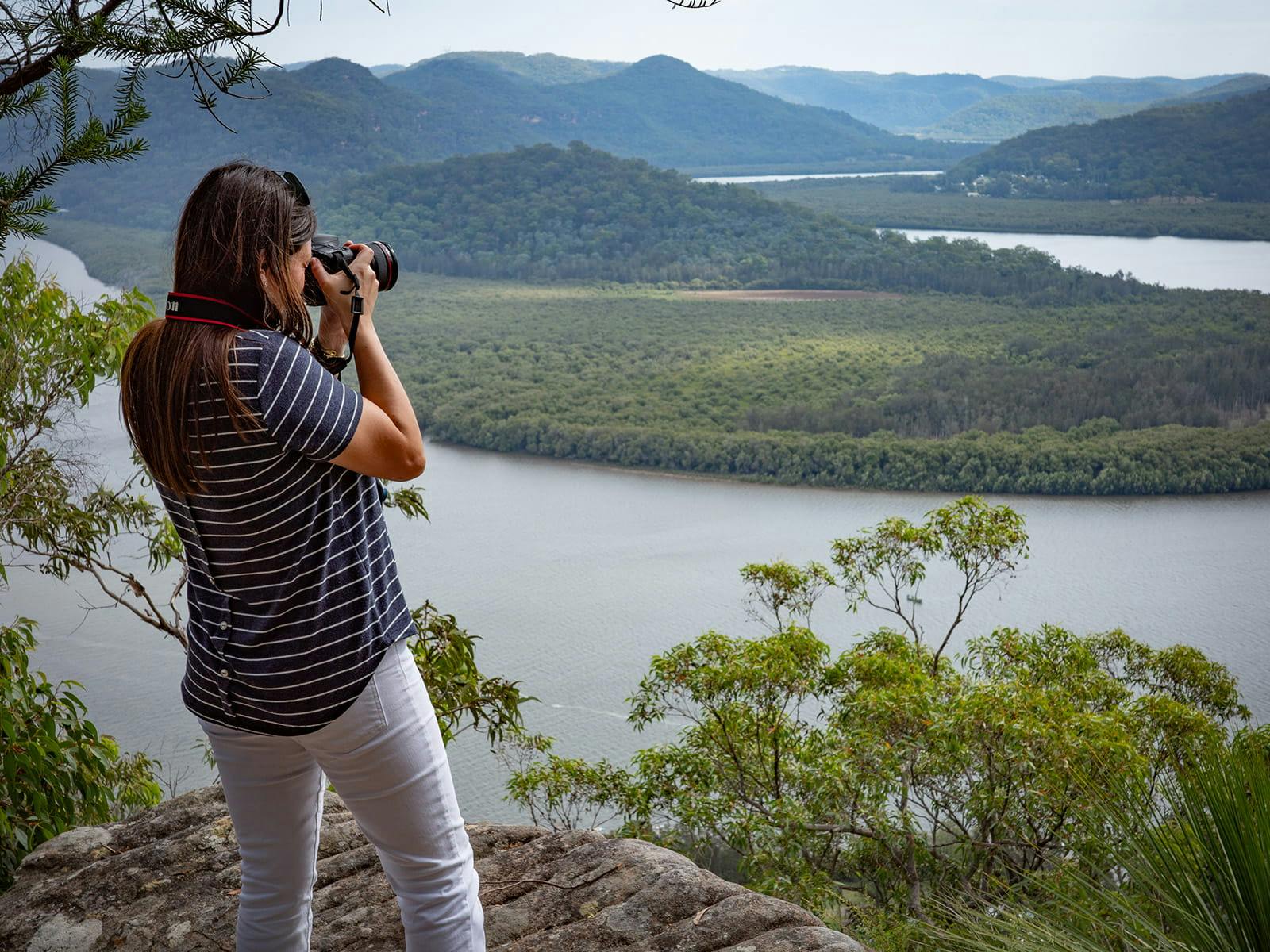 Woman photographing river valleys and forested landscapes from a scenic lookout in Australia.
