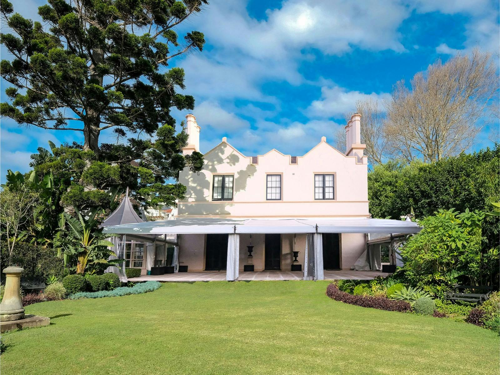 Historic mansion from the 1800s surrounded by gardens and a lush lawn.