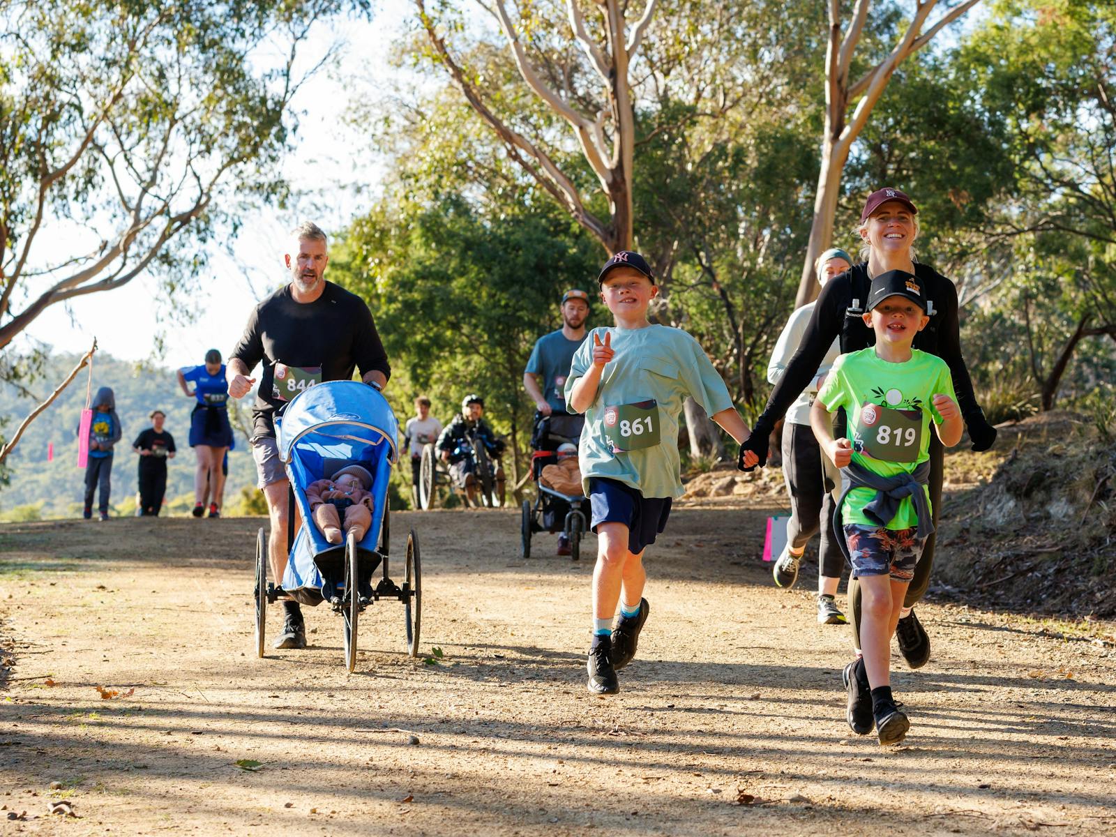 Young boys run with their parent while another runner runs with a child in a pram