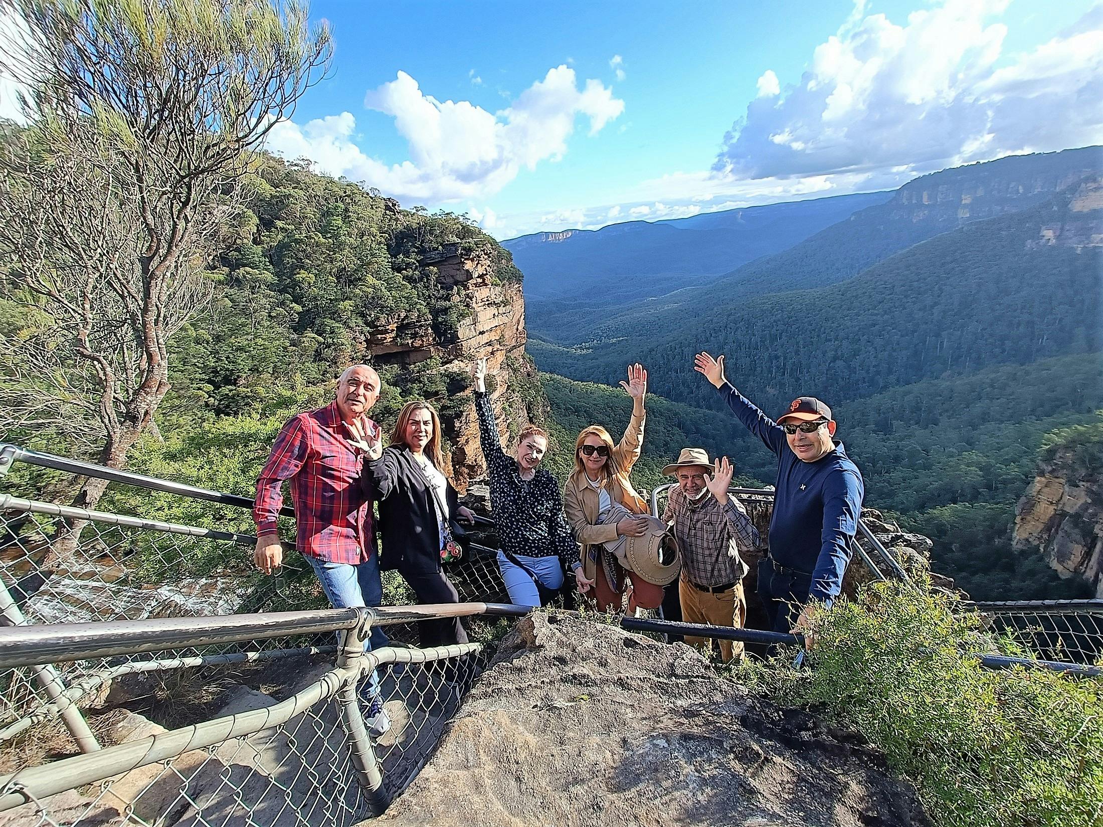 6 adults waving at camera with mountain views behind them