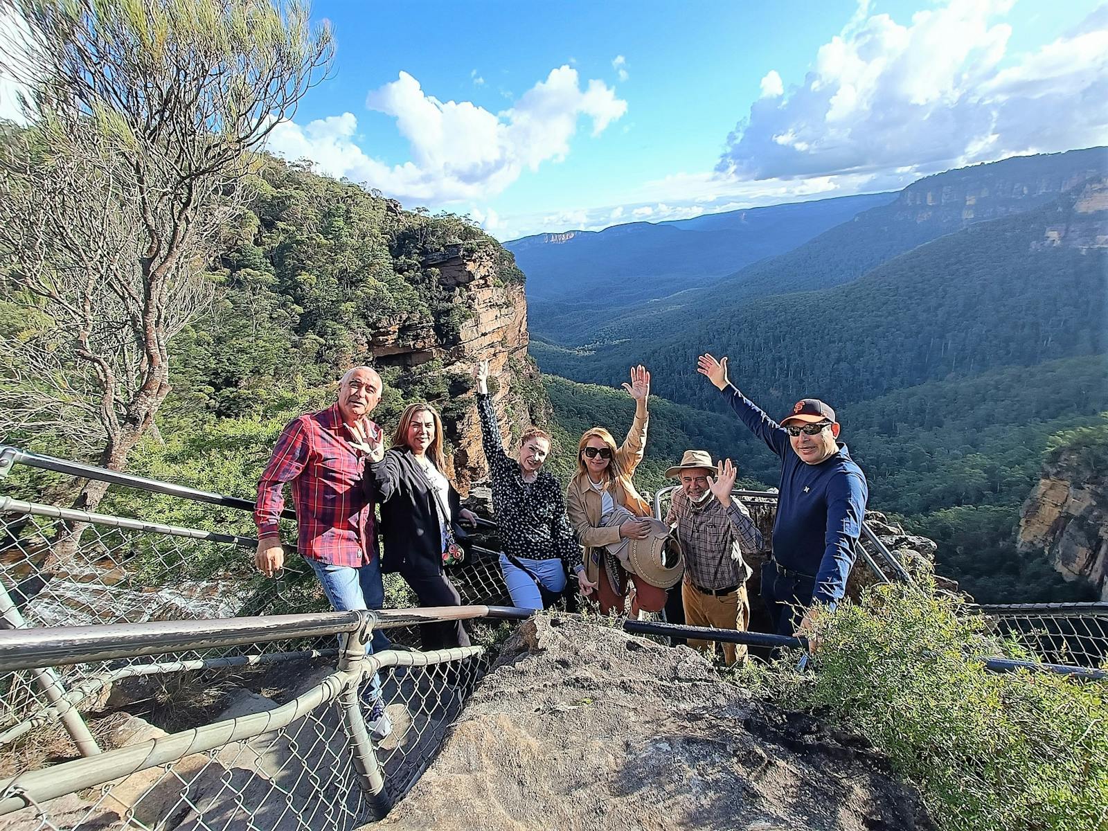 6 adults waving at camera with mountain views behind them