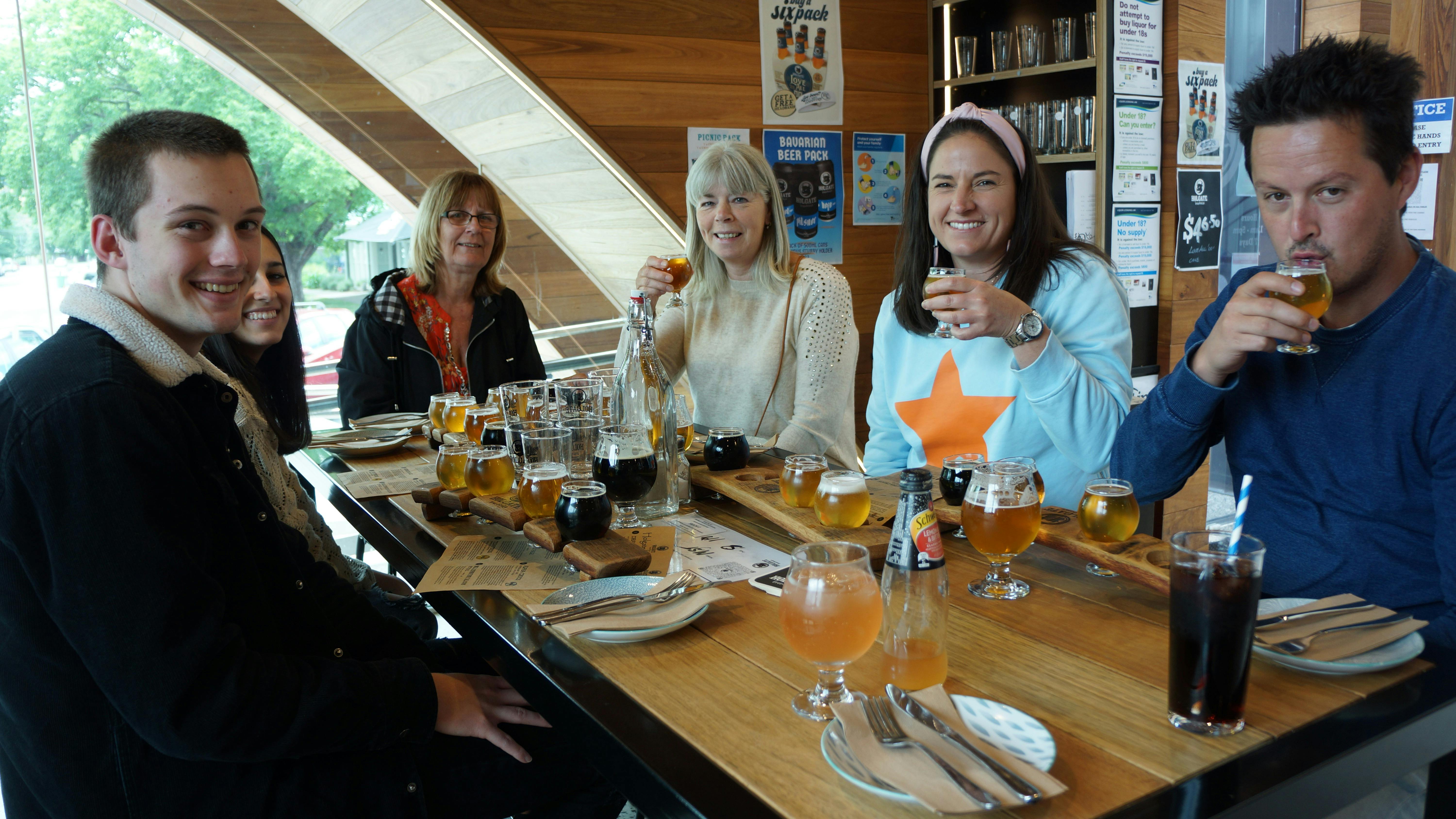 A group of men and women sitting around a table with food and paddles of beer