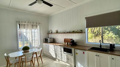 A bright kitchen with sun shining, white cabinets, fridge, microwave, oven, sink, and dining table.