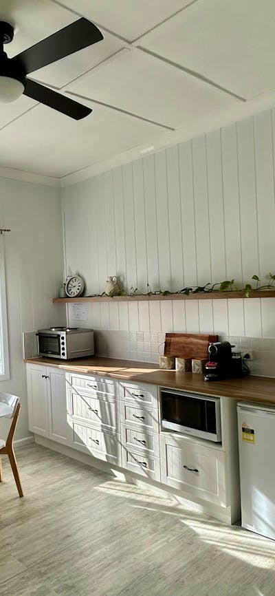 A bright kitchen with sun shining, white cabinets, fridge, microwave, oven, sink, and dining table.