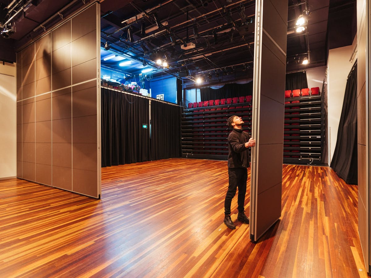 A black box theatre with retractable  200 seat seating bank Staff removing the dividing wall .