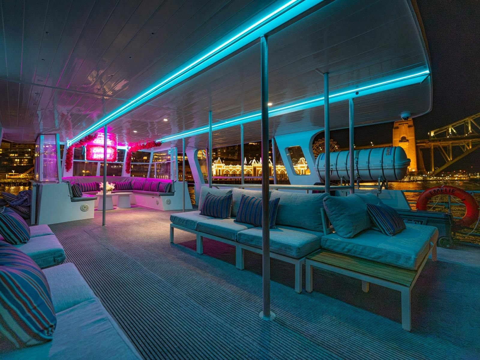 Upper deck of Capri on Emelie at night with mood lighting and the Harbour Bridge behind