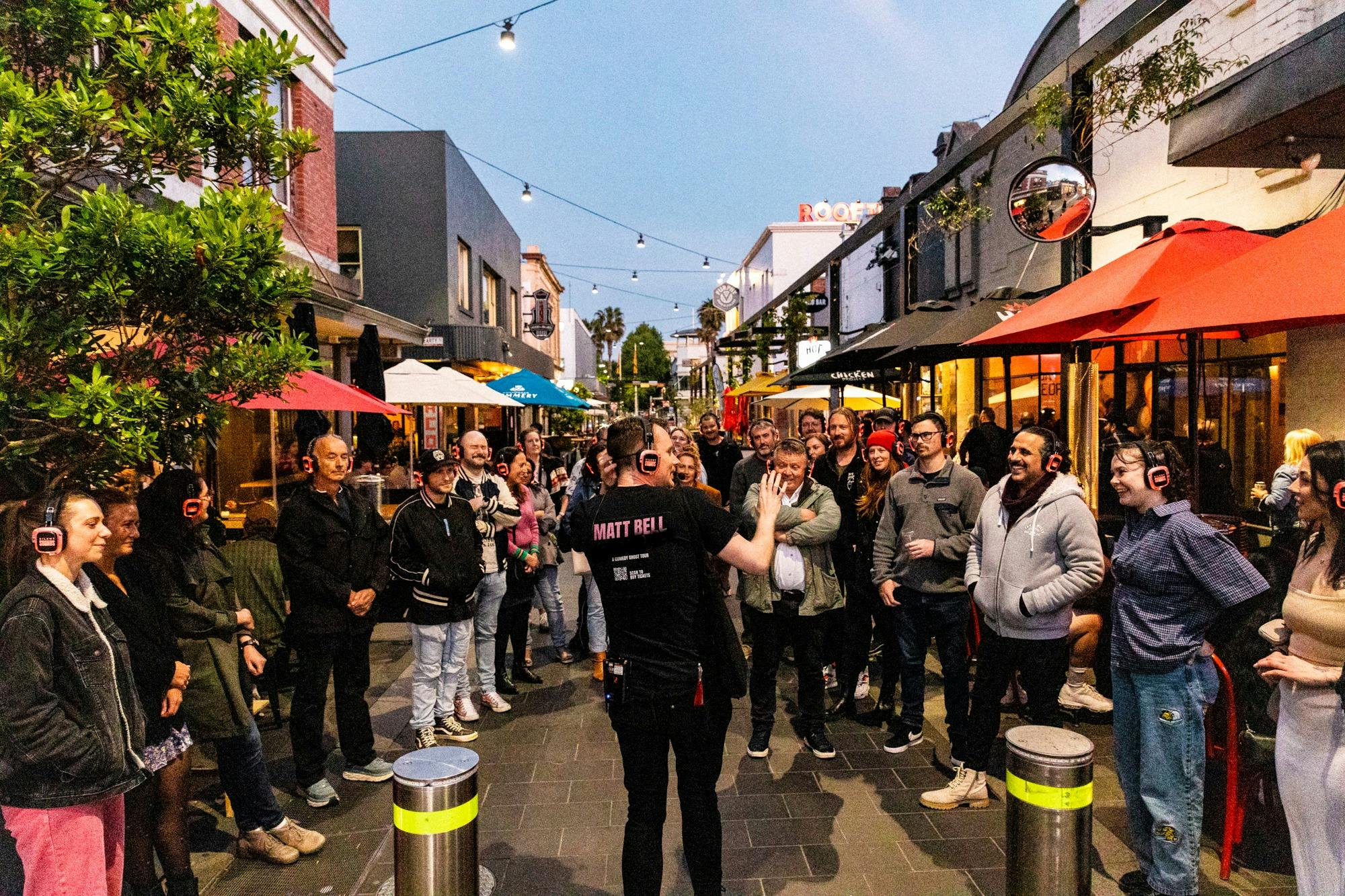 Man in black t-shirt talking to an audience with a terrified look on his face
