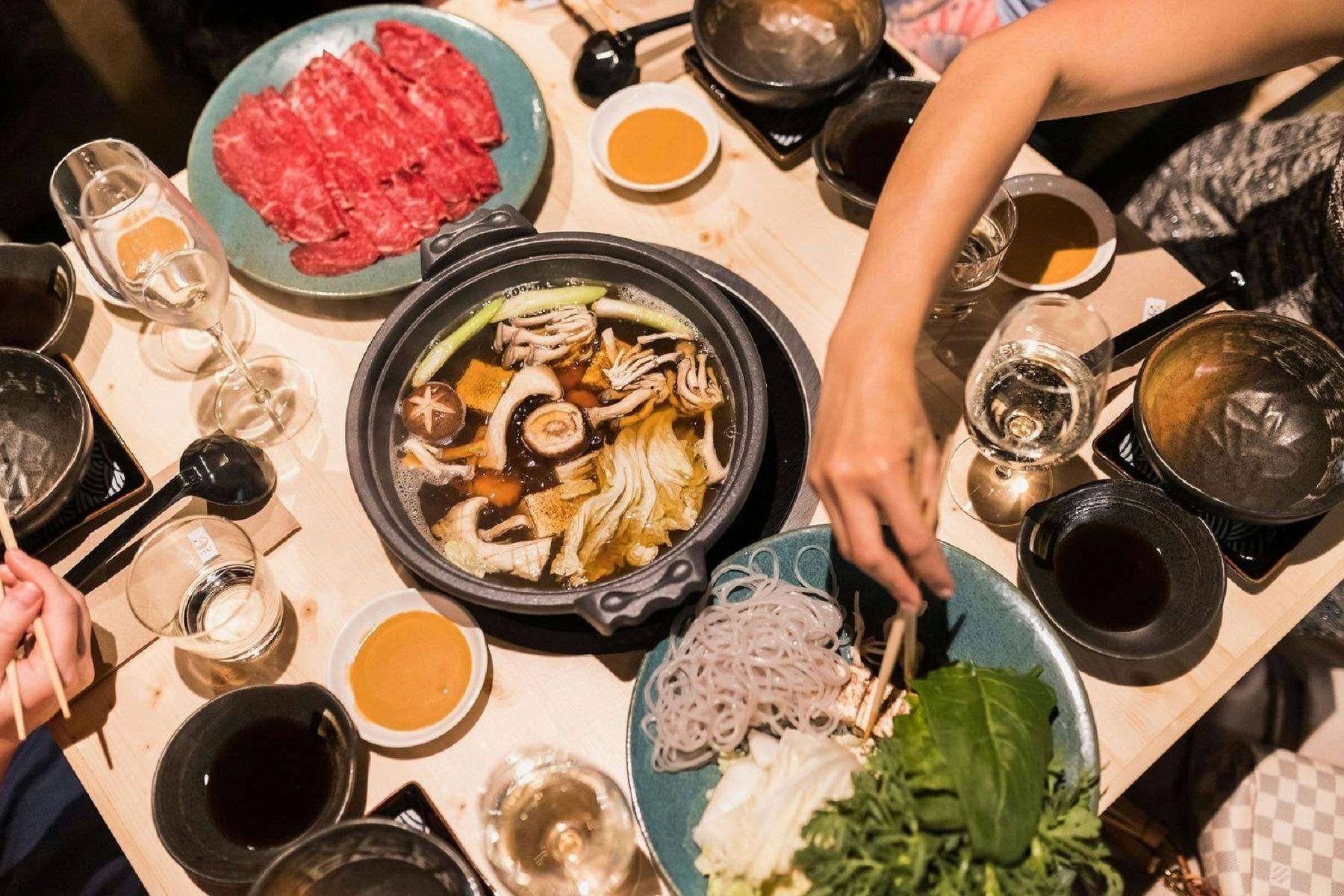 Range of Japanese dishes and hotpot with a person reaching across with chopsticks