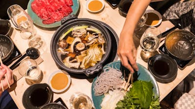 Range of Japanese dishes and hotpot with a person reaching across with chopsticks