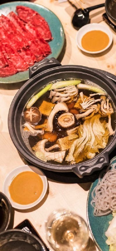 Range of Japanese dishes and hotpot with a person reaching across with chopsticks