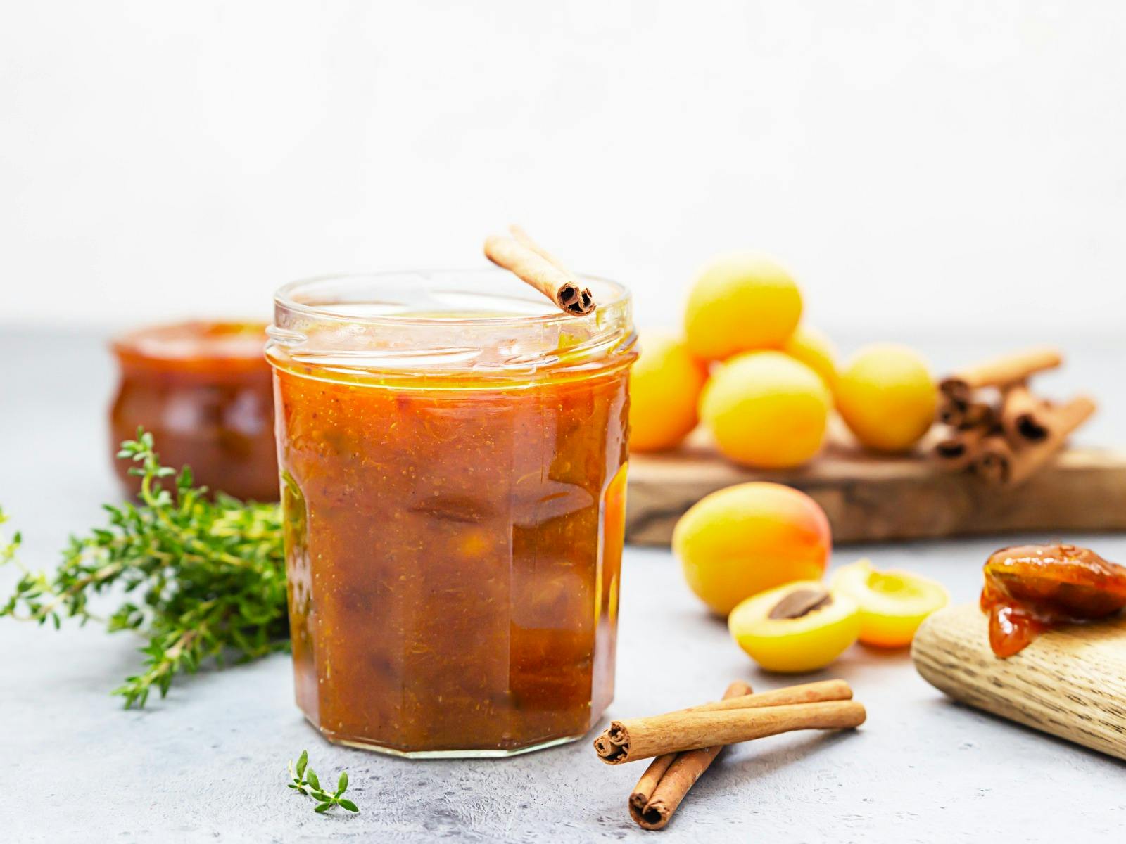 Apricot jam in a glass jar, fresh apricots, thyme and cinnamon on grey background
