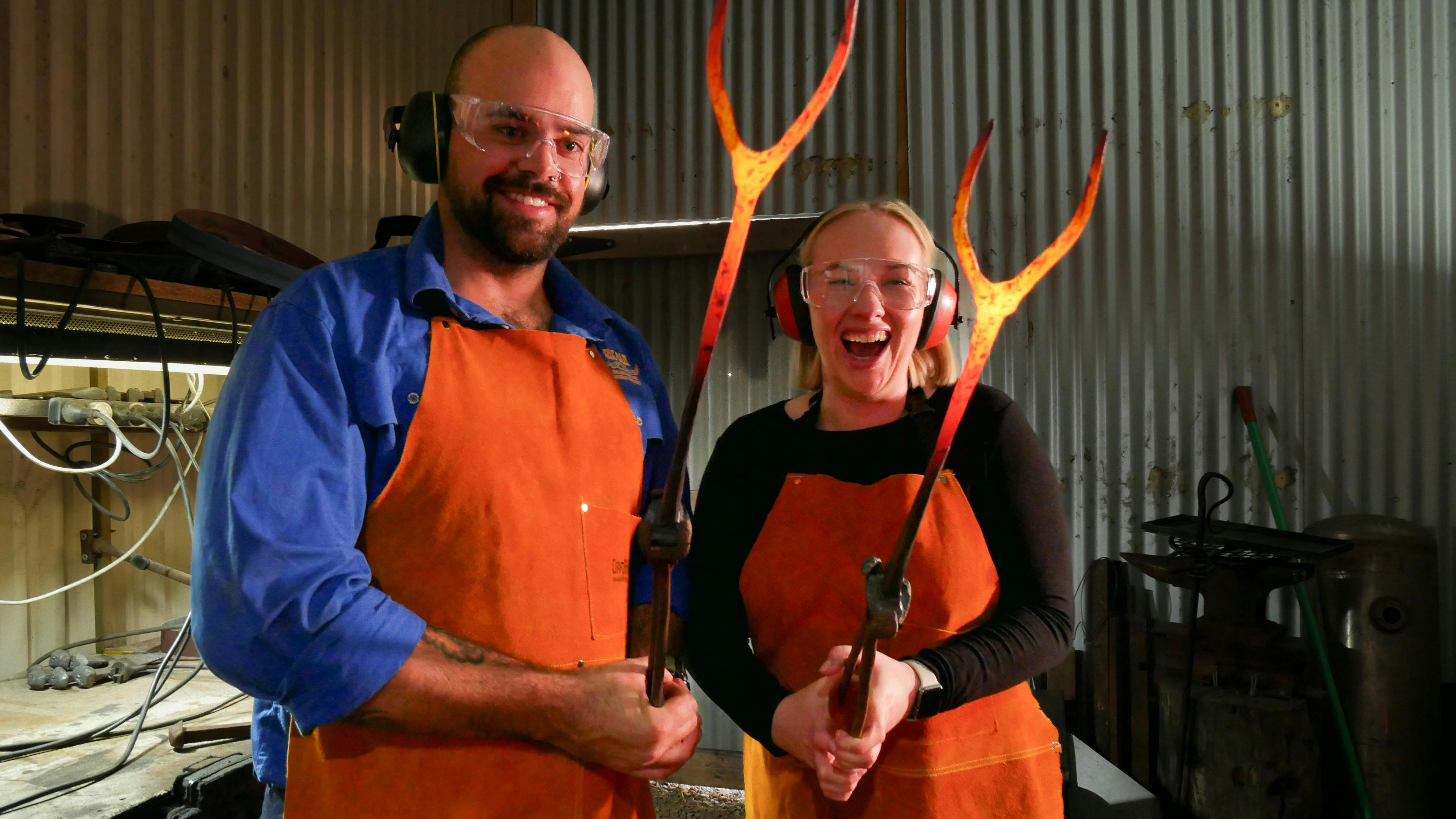 two participants holding red hot marshmallow roasters that they made in the Blacksmith Experience