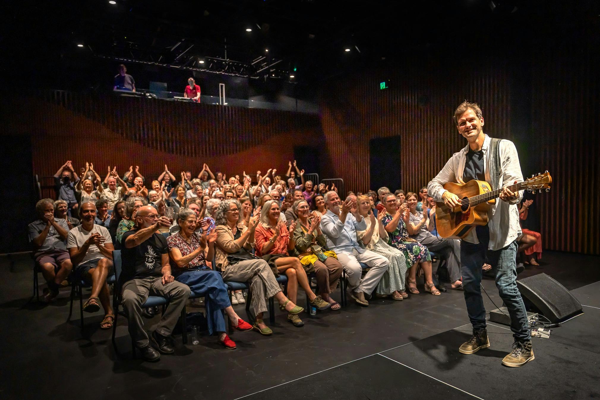musician with guitar on stage with audience in background - interior of the theatre