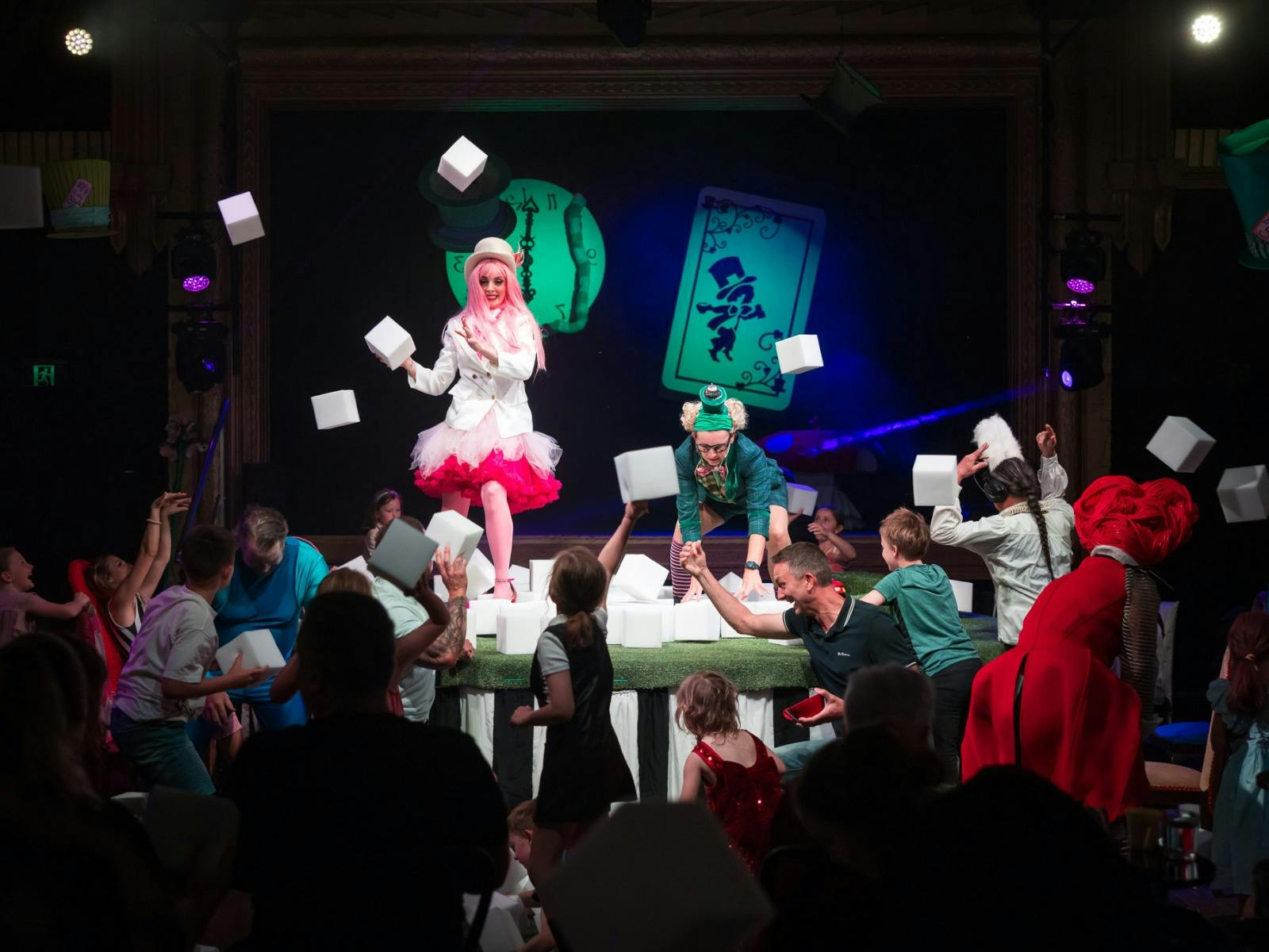 Children in the audience throw white foam cubes at the performers on stage
