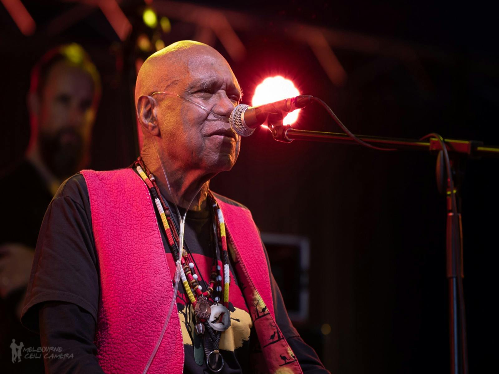 Uncle Archie roach sings on stage, wearing a black shirt and red waistcoat