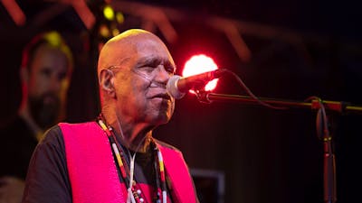 Uncle Archie roach sings on stage, wearing a black shirt and red waistcoat