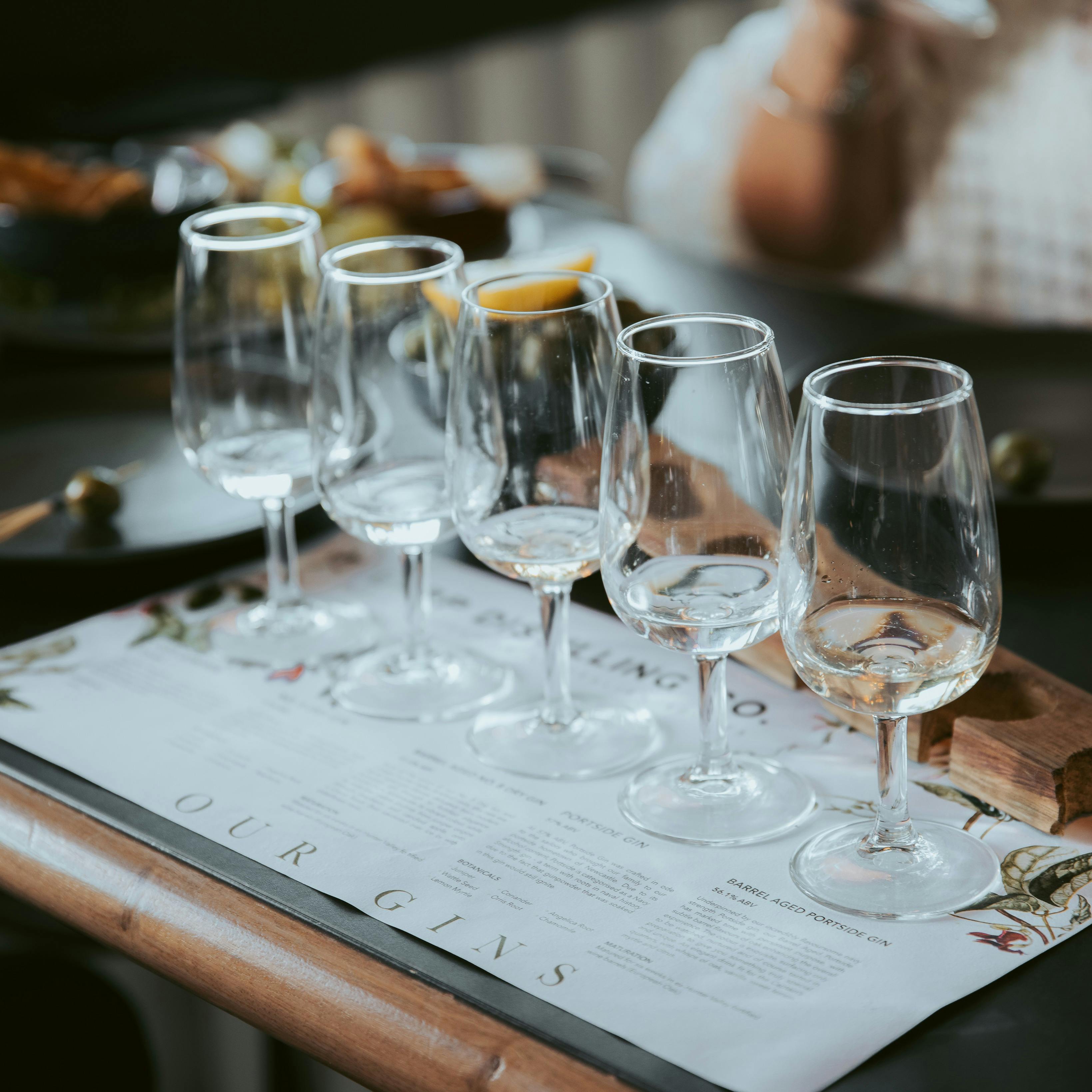 Five tasting glasses with sample spirits sit on an information placemat, each paired with its detail