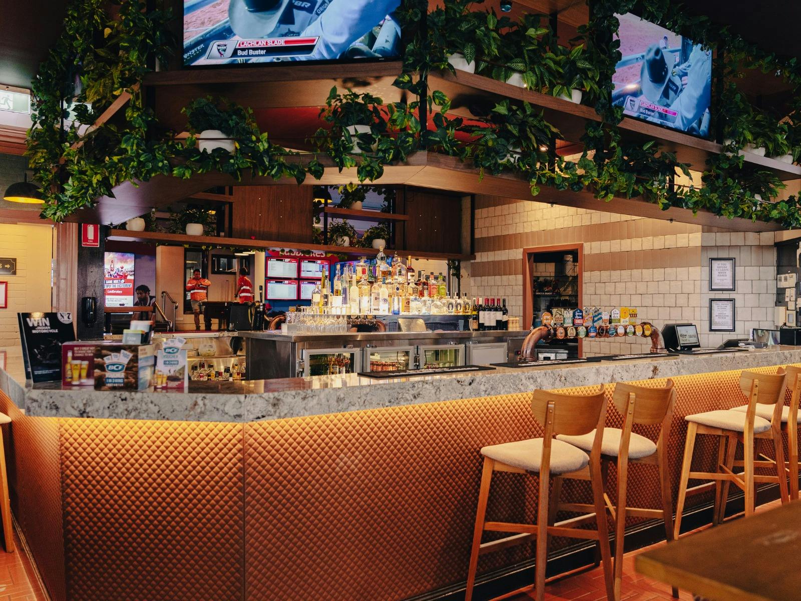 Inside photo of The Spotted Cow bar. Tv screens above bar and wooden seating along the bar