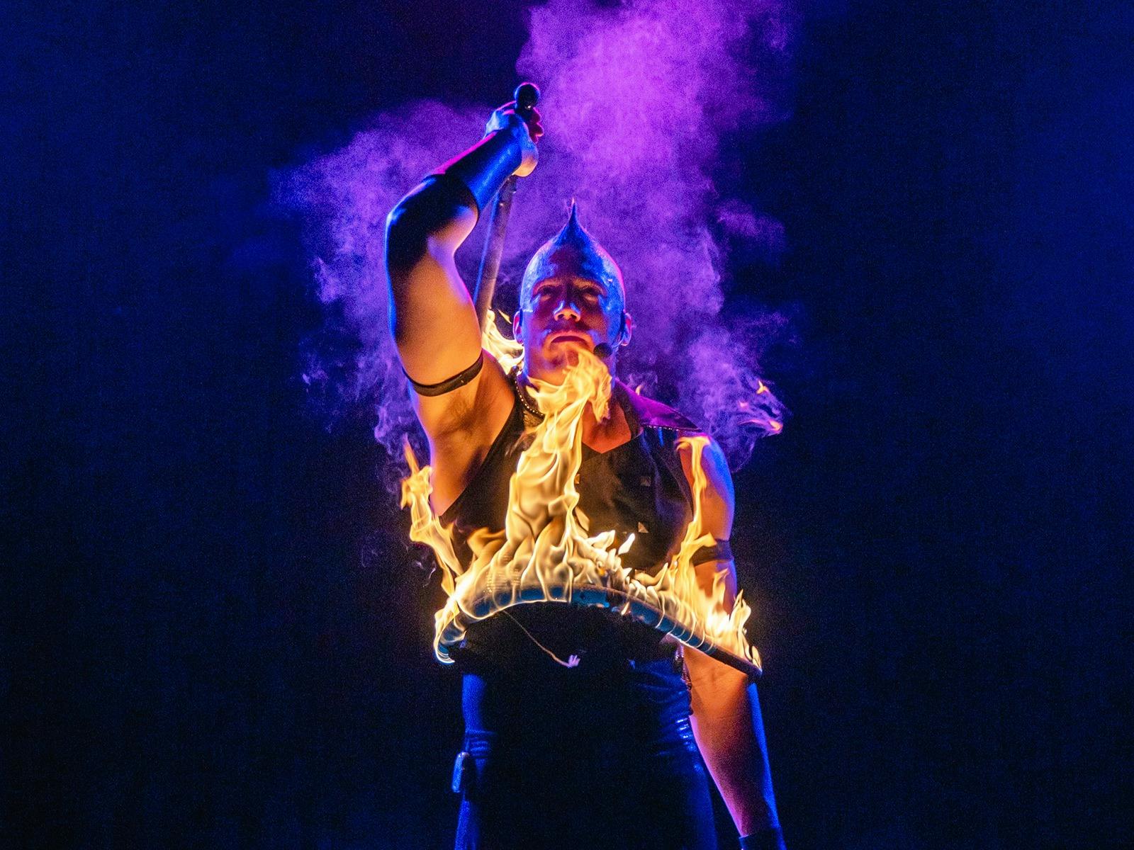 A circus performer holds a fire lasso around their body