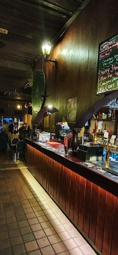Tables and bar stools line the wall on the left, with a brightly lit bar with red tiles on the right