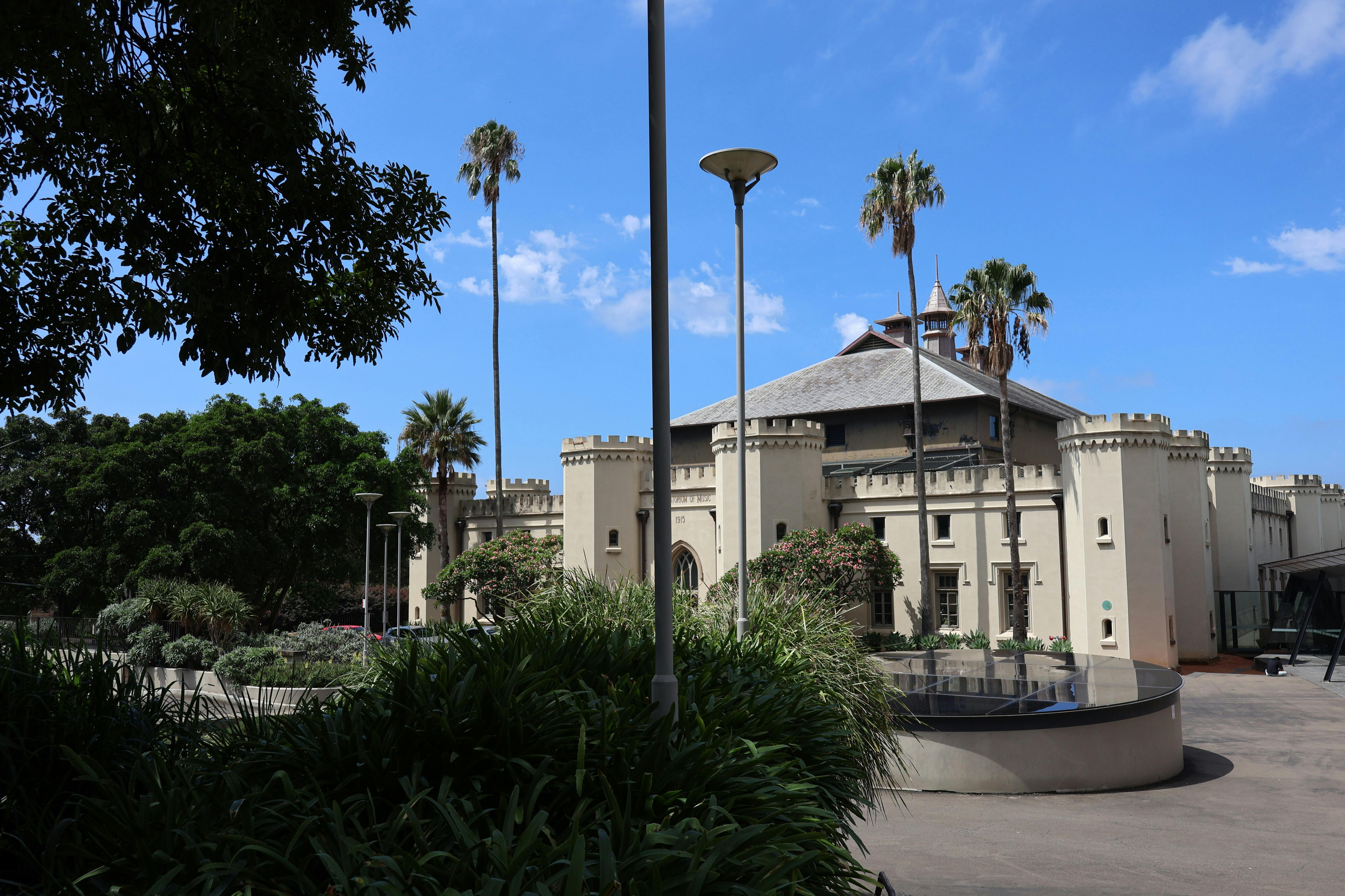 A white building with turrets, bordered by plants