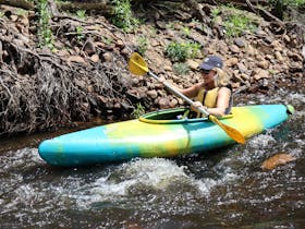 A young woman paddling down the river in a single kayak