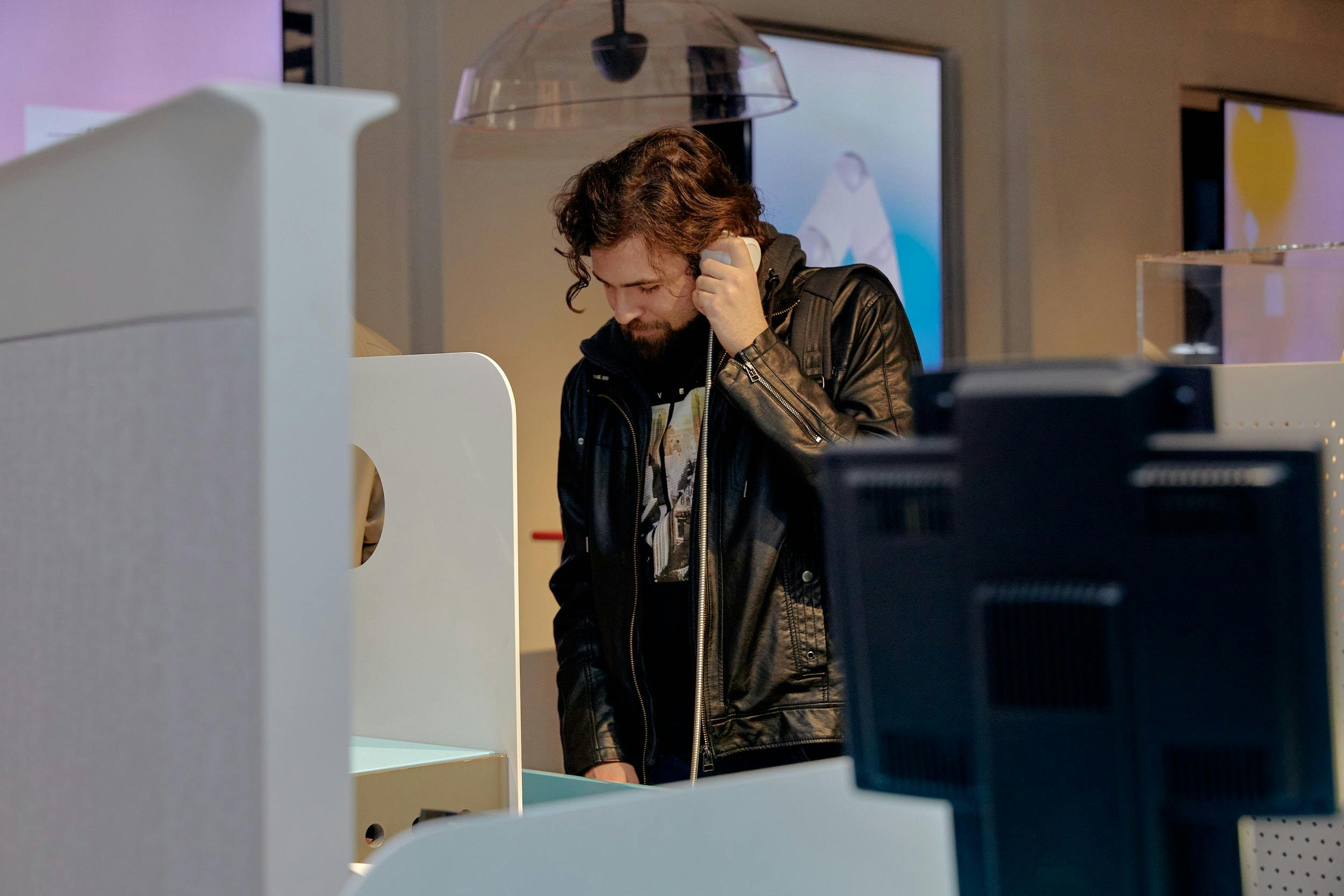 A man listens to a handheld earpiece by a desk display.