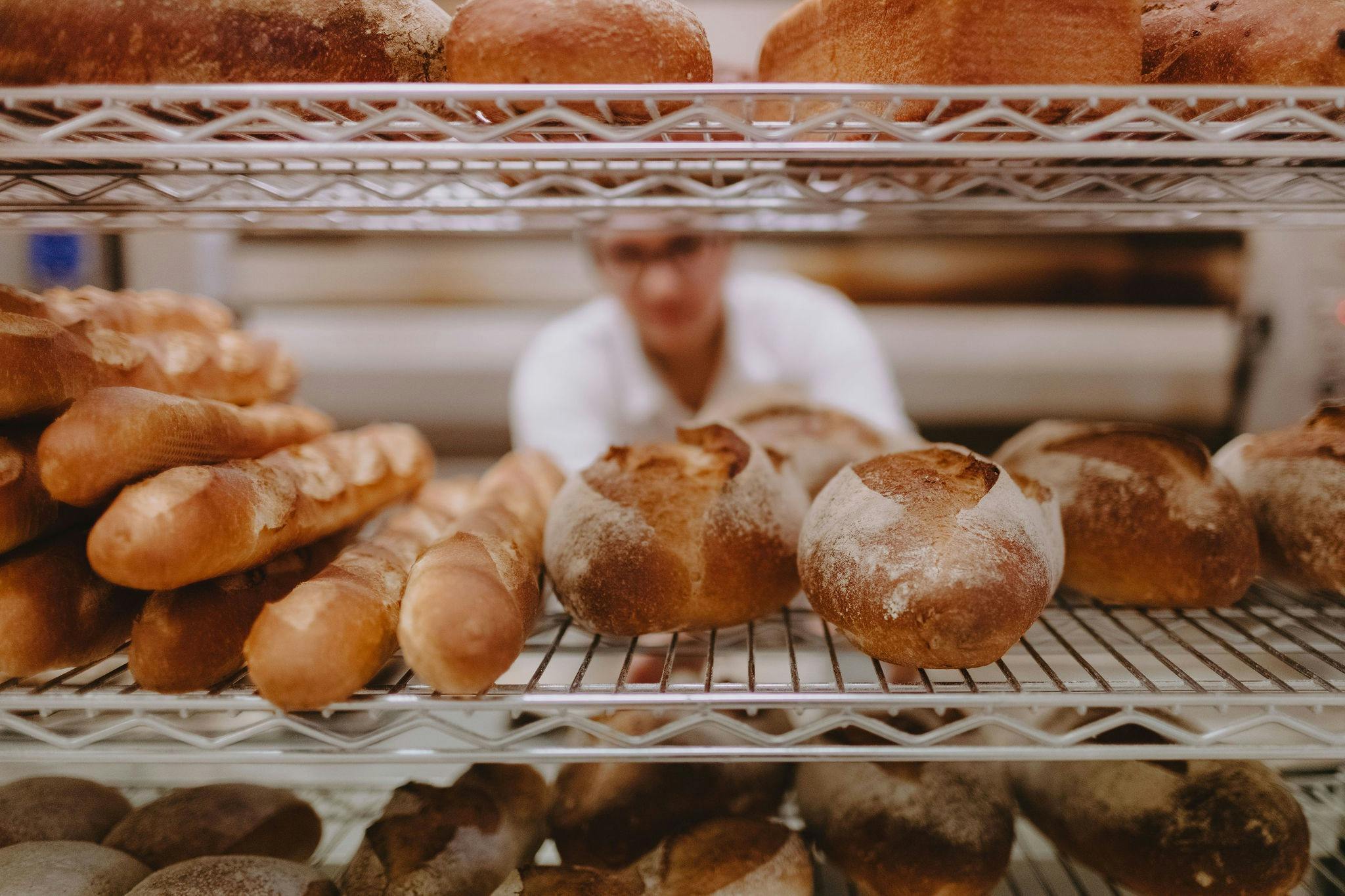 Freshly baked baguettes stacked up on a shelf with the baker admiring their work in the background