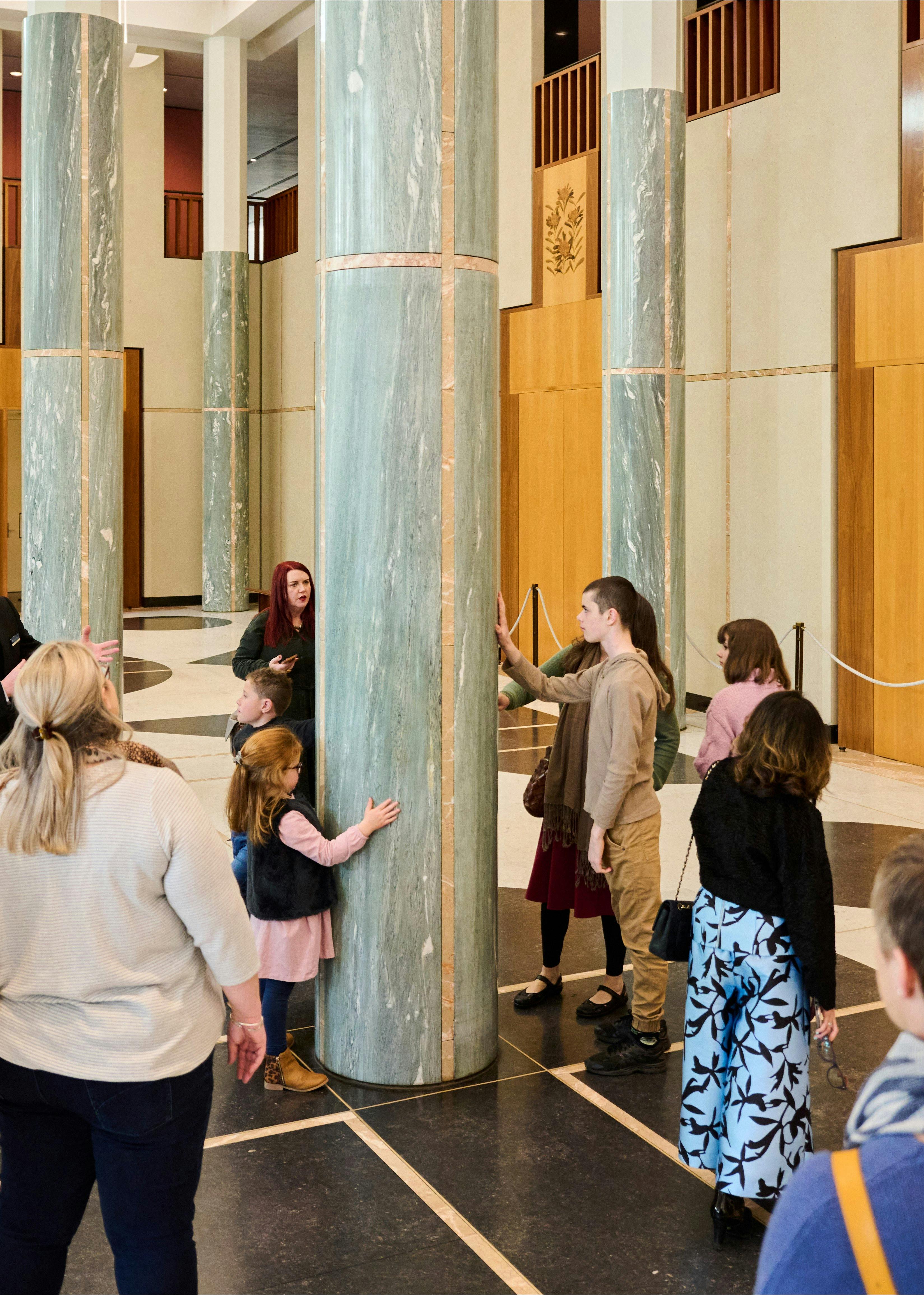 Tour participants in the Marble Foyer of Parliament House interact with one of the marble pillars