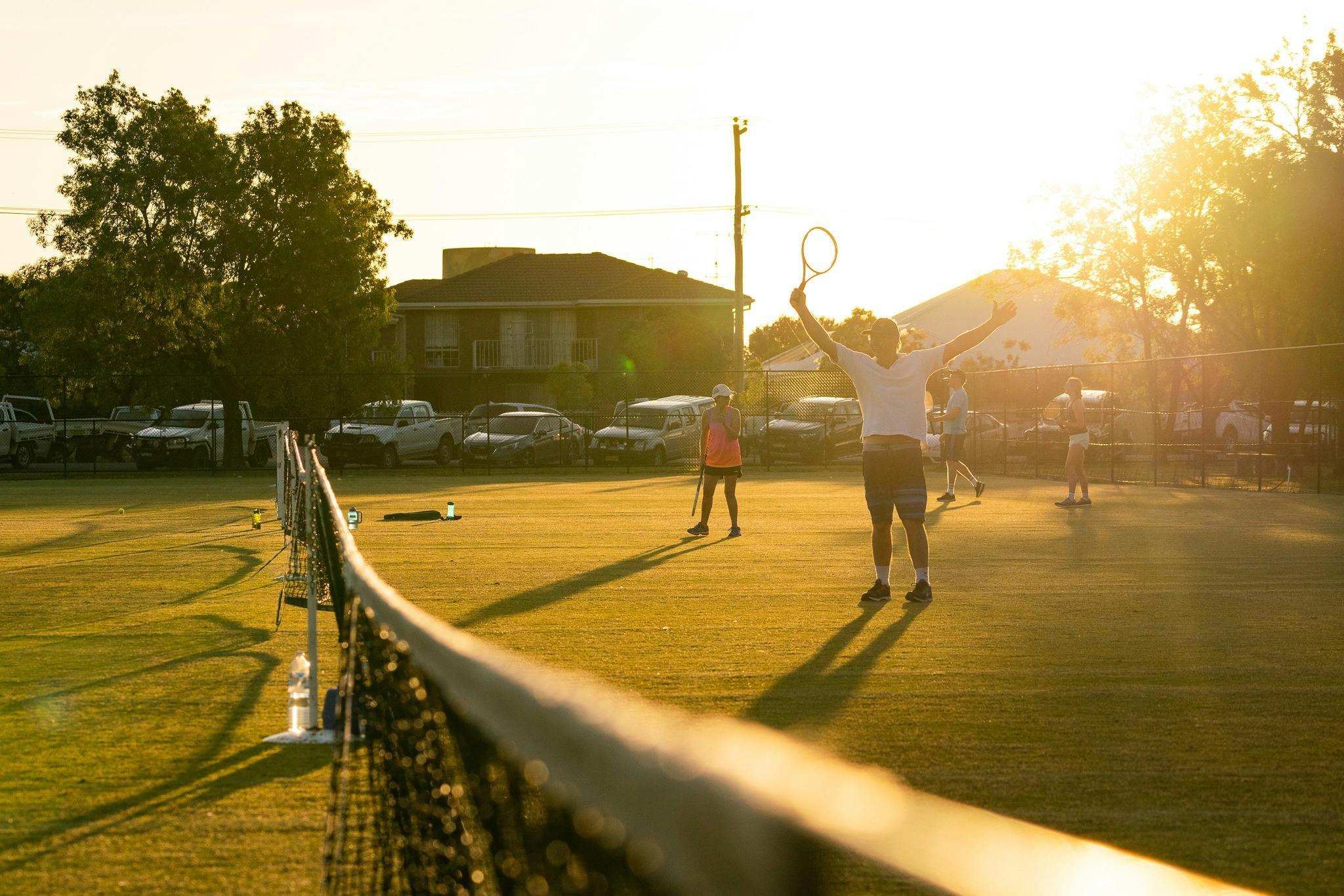 A tennis net in the foreground, a silhouette of someone serving in the background