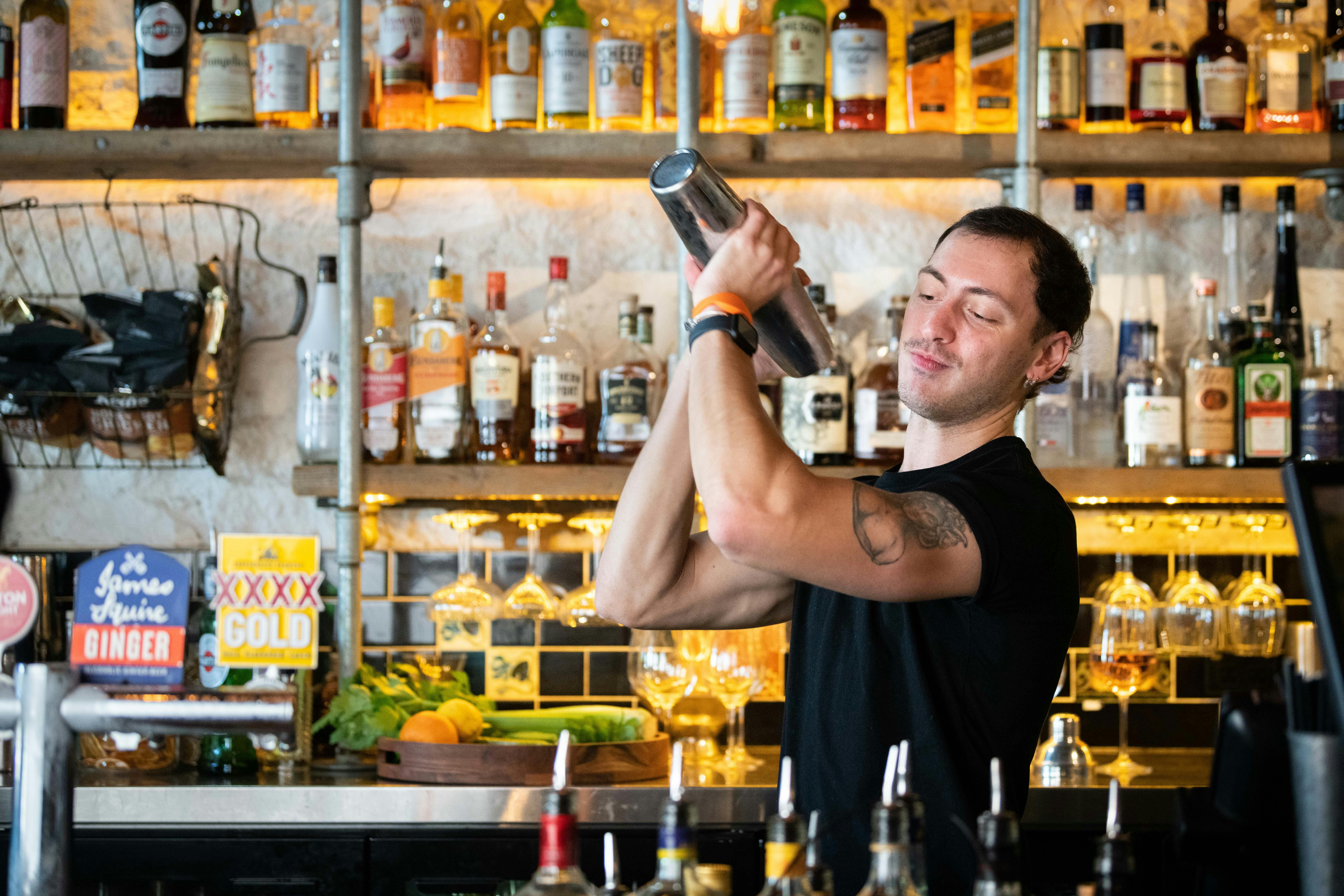 Bartender shaking up a cocktail in front of a wall of alcoholic mixers.