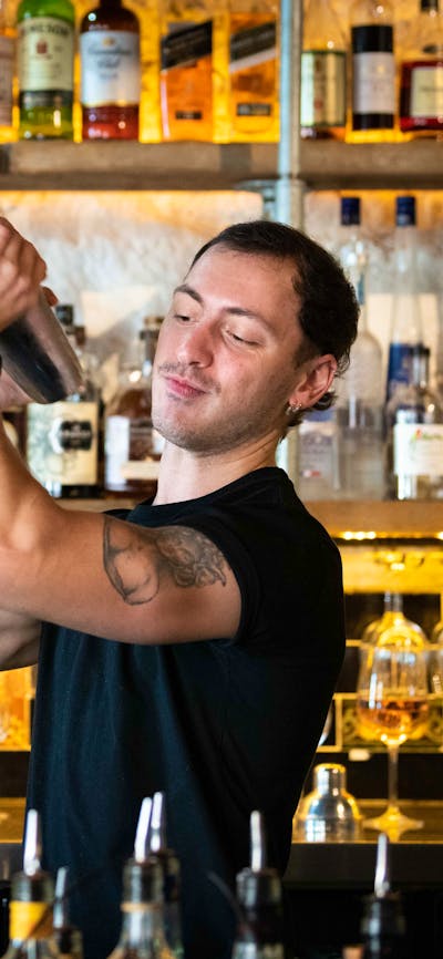 Bartender shaking up a cocktail in front of a wall of alcoholic mixers.
