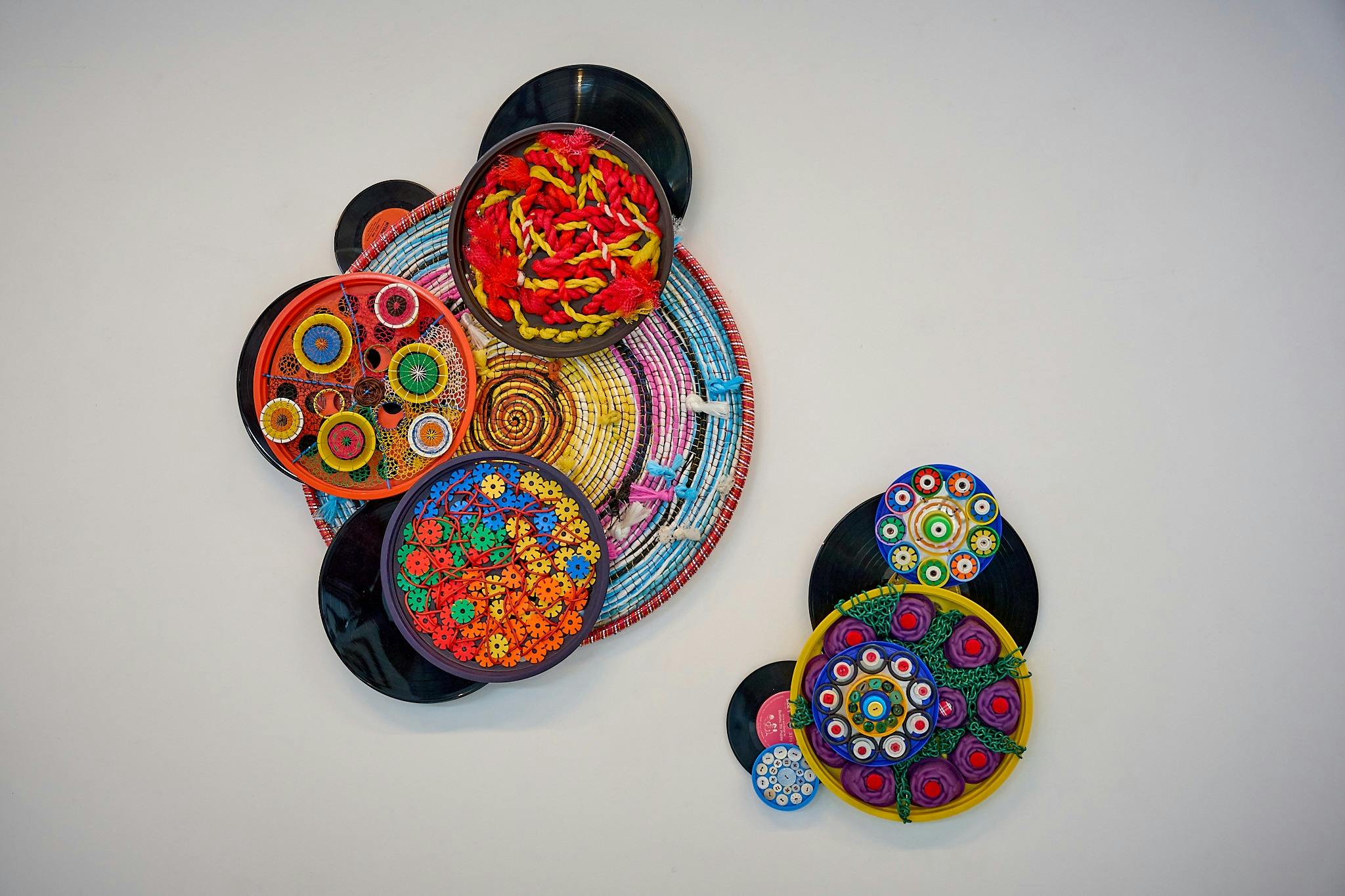 Two circular textile artworks hang on a white wall.  One is larger, and both feature bright colours.