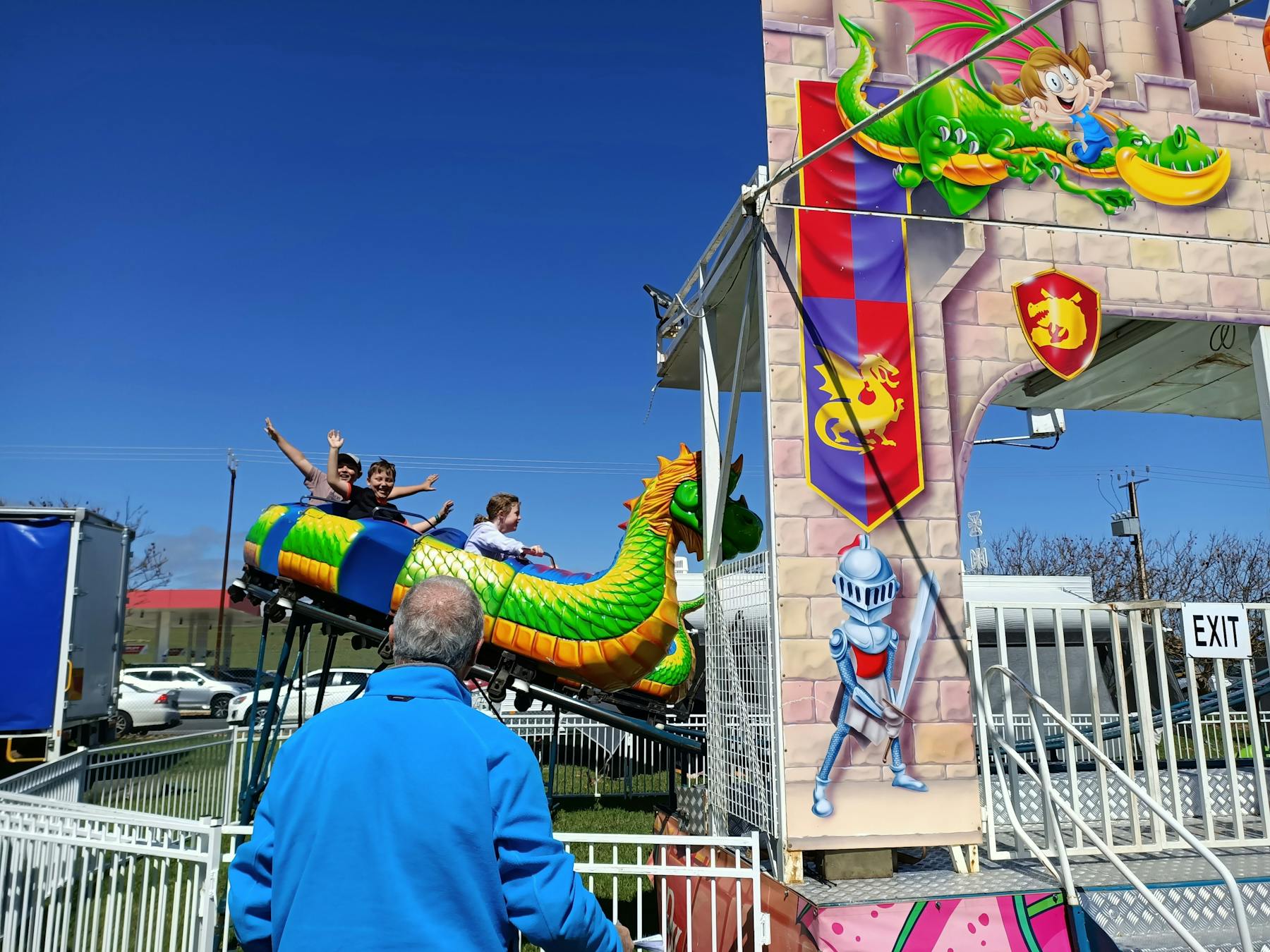 Fairground ride that is a green and orange dragon carriage with mediaeval castle gateway in front