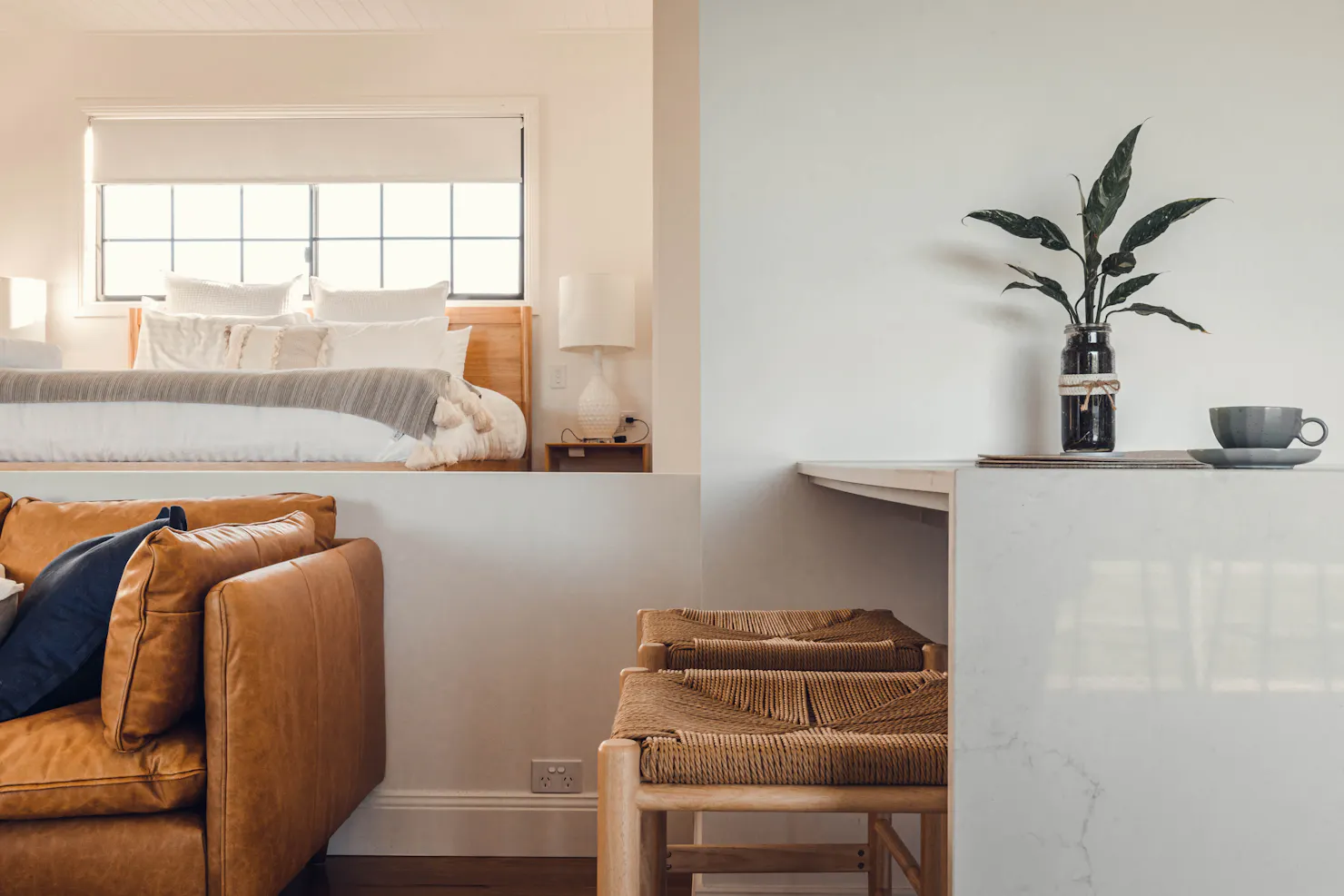 Tan leather lounge, bar stools at breakfast bench. King bed with natural light from large window.