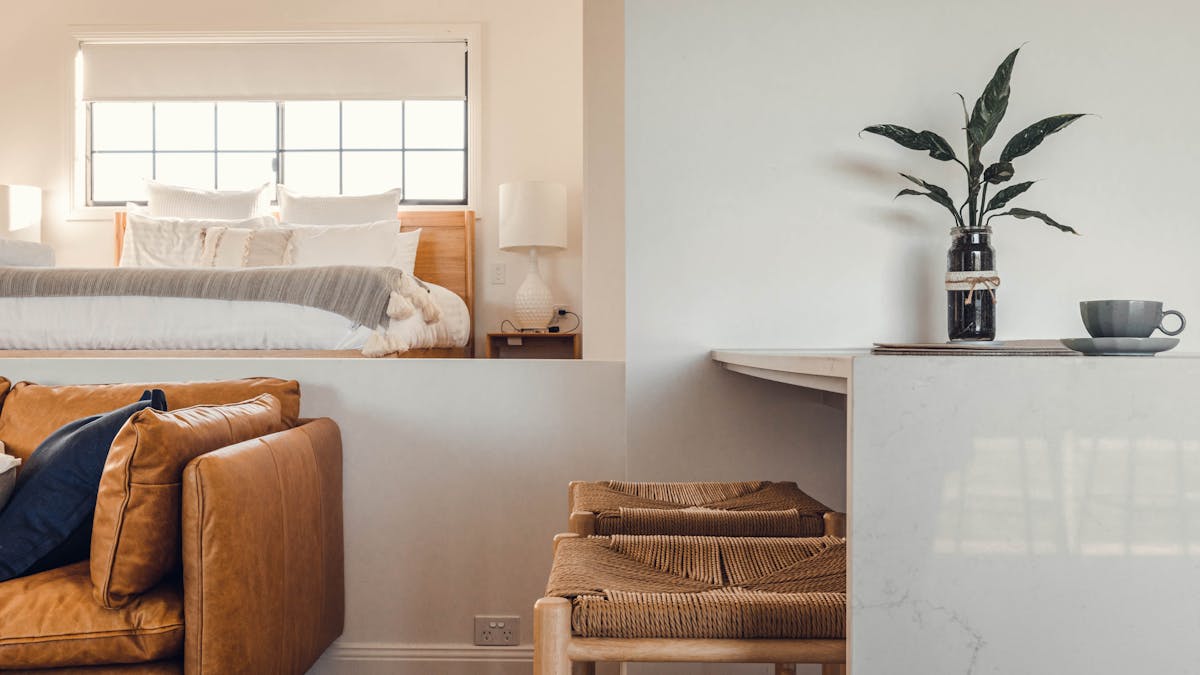 Tan leather lounge, bar stools at breakfast bench. King bed with natural light from large window.