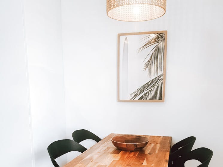 Dining table with chairs, photo of palms on the wall, light shade above