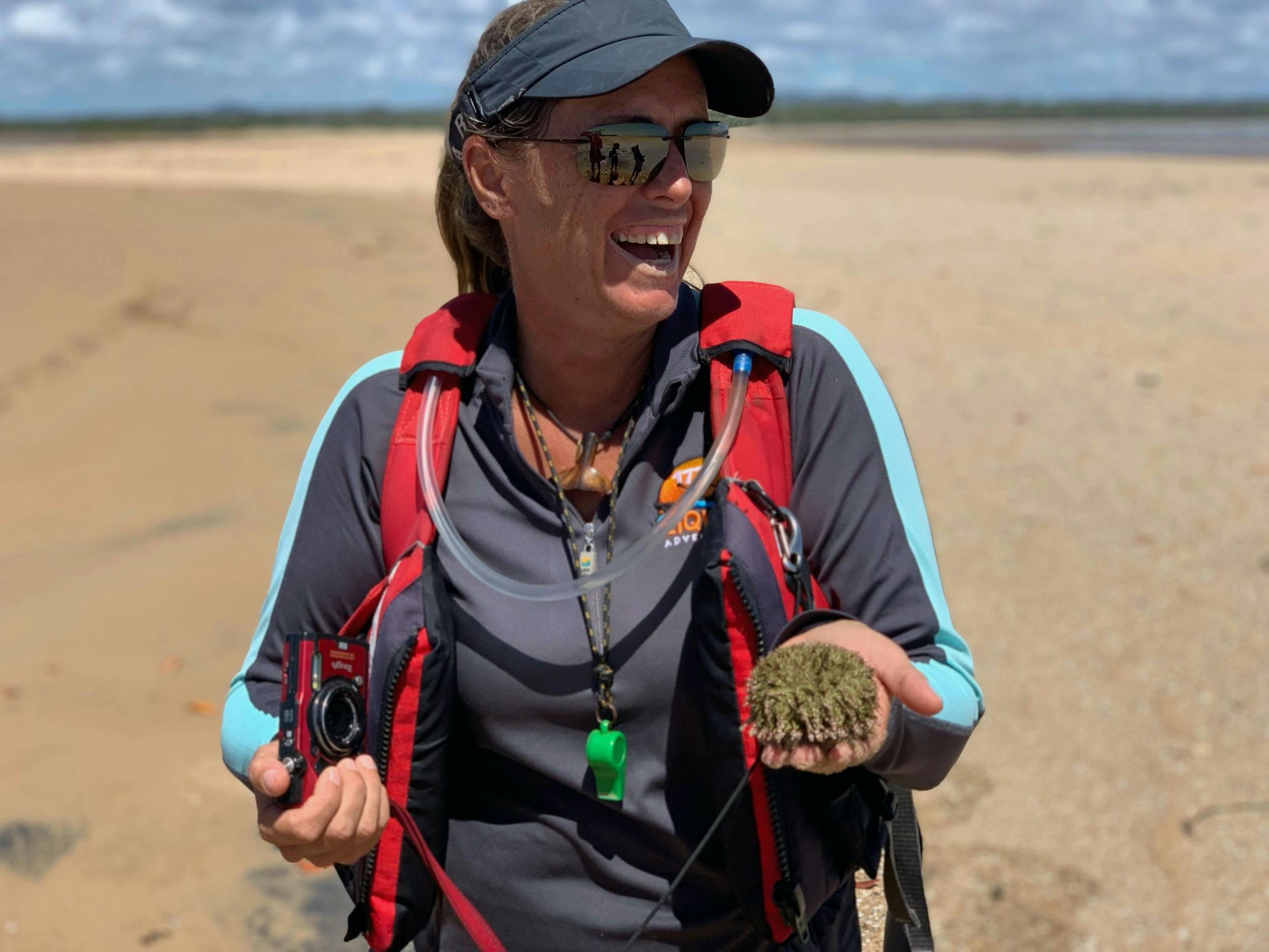 Tour guide Janina wearing a red life jacket, holding a sea urchin and laughing