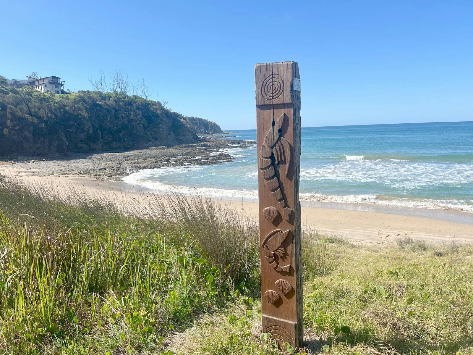 A timber post on a beach carved with aboriginal designs