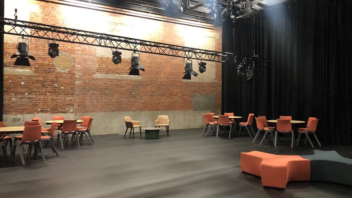 Blackbox theatre with cabaret table and chairs seating, curtains and brick wall at front of theatre.