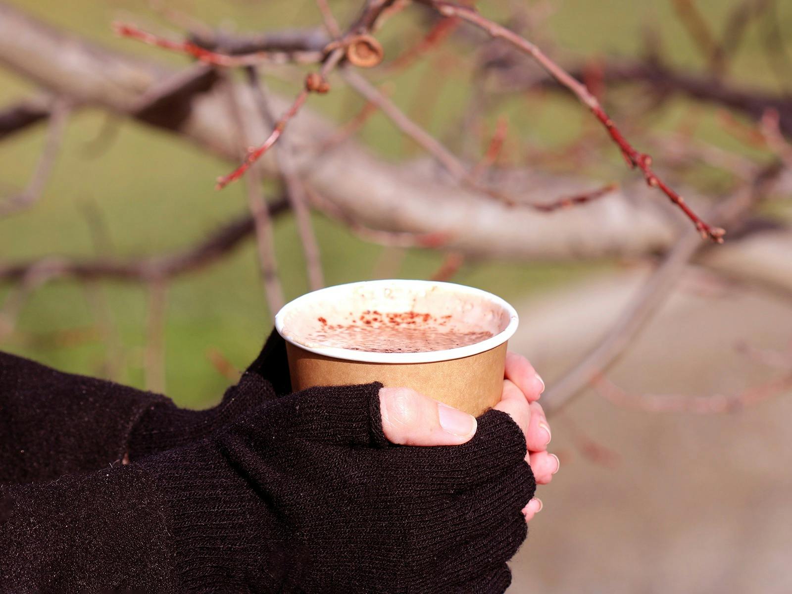 A pair of gloved hands clasp a disposable mug of hot chocolate