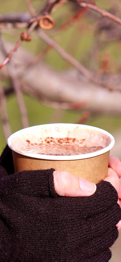 A pair of gloved hands clasp a disposable mug of hot chocolate