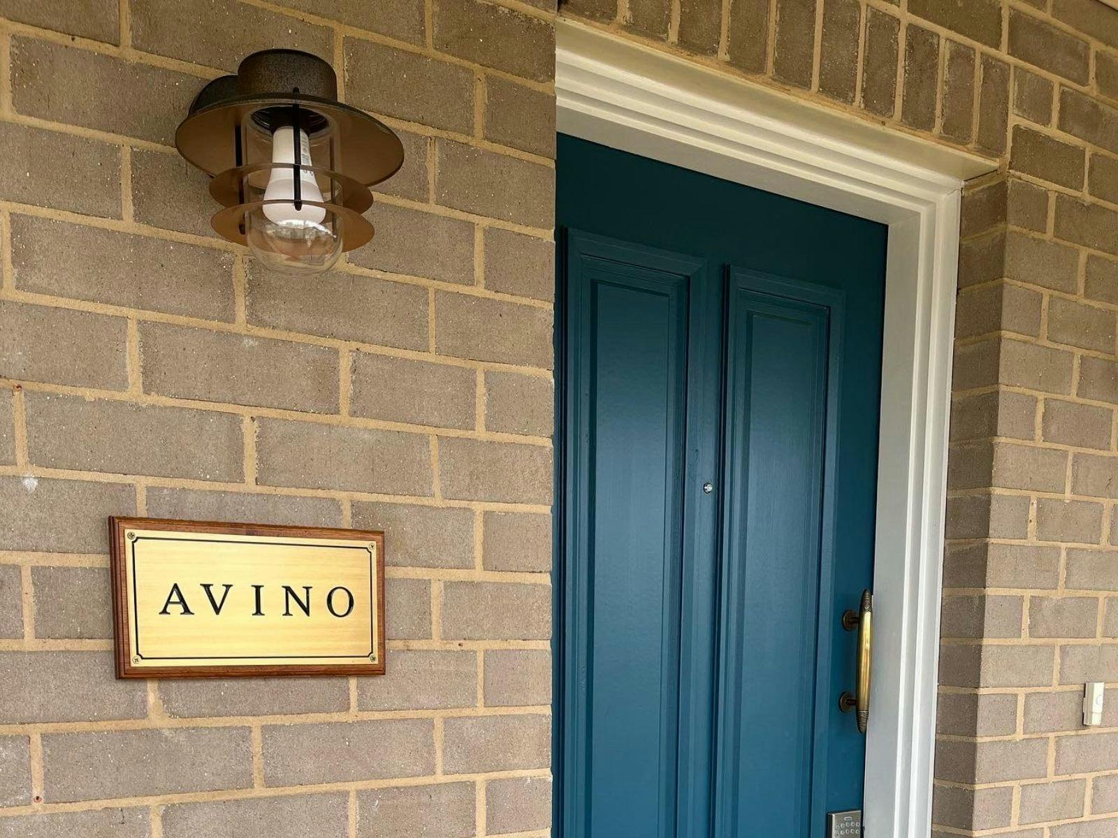 A blue front door with brass handle. An outdoor light sits above a brass plaque that says Avino