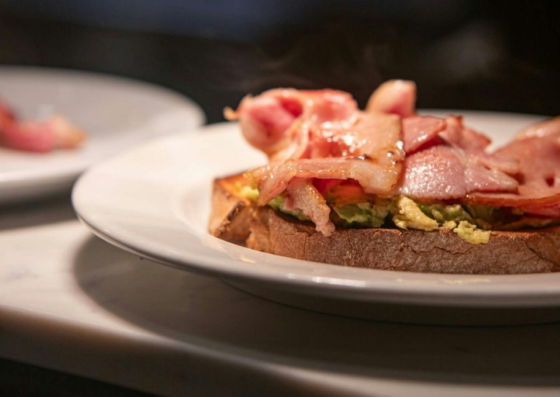 A sample dish shown on a plate with a black background containing bacon on toast.