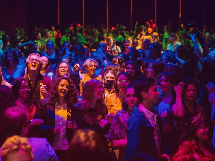 a photo of a crowd laughing and smiling in an indoor venue with multicoloured lights