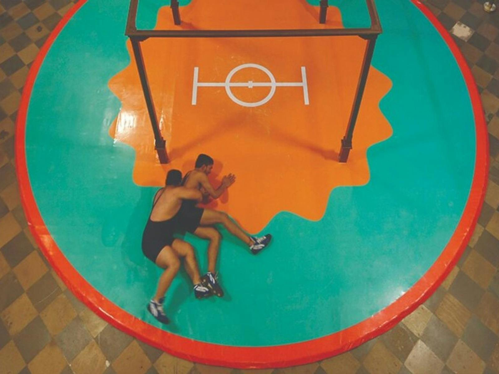 two men wrestle on a large circular mat, which is orange and green